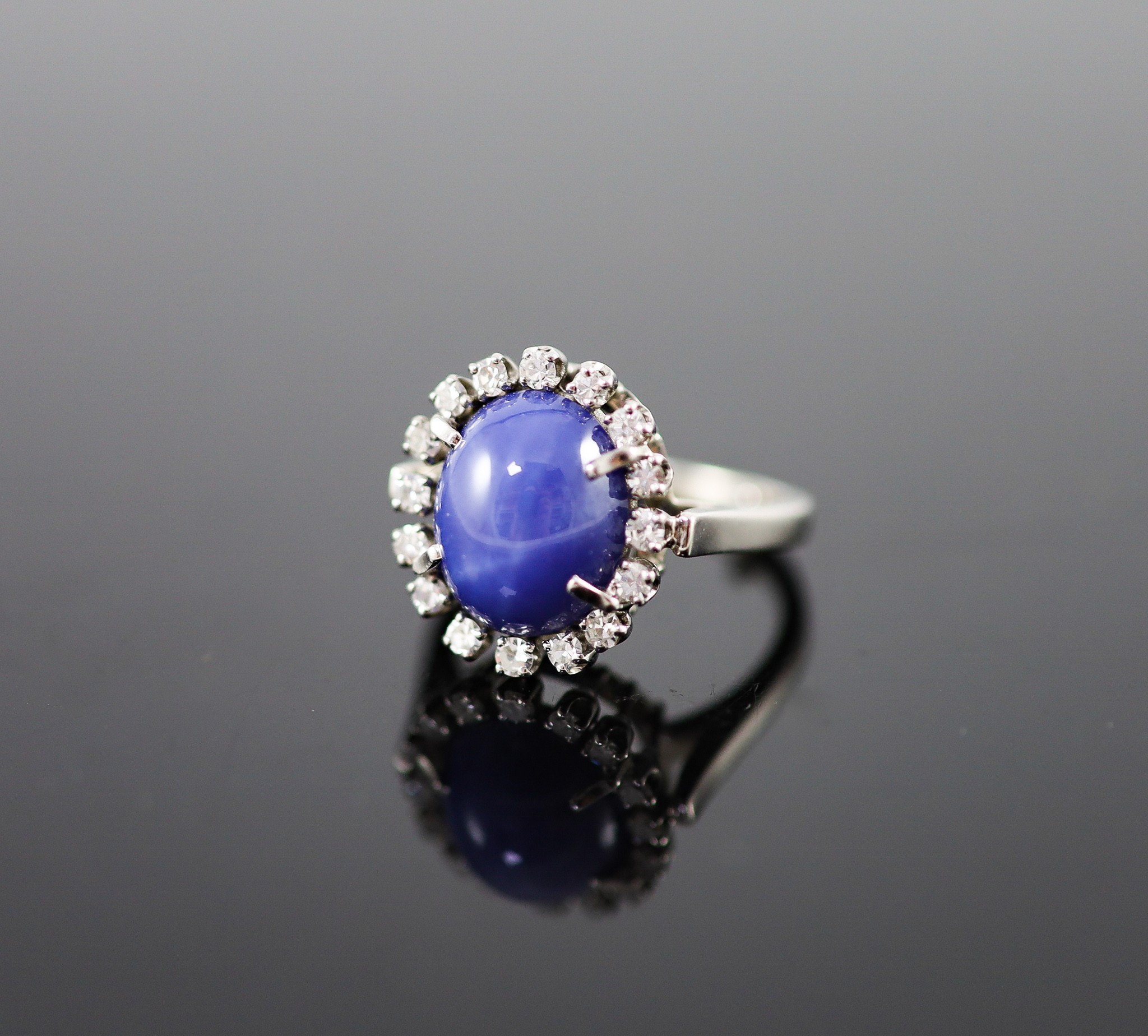A 14k white gold, cabochon star sapphire and diamond set oval cluster ring